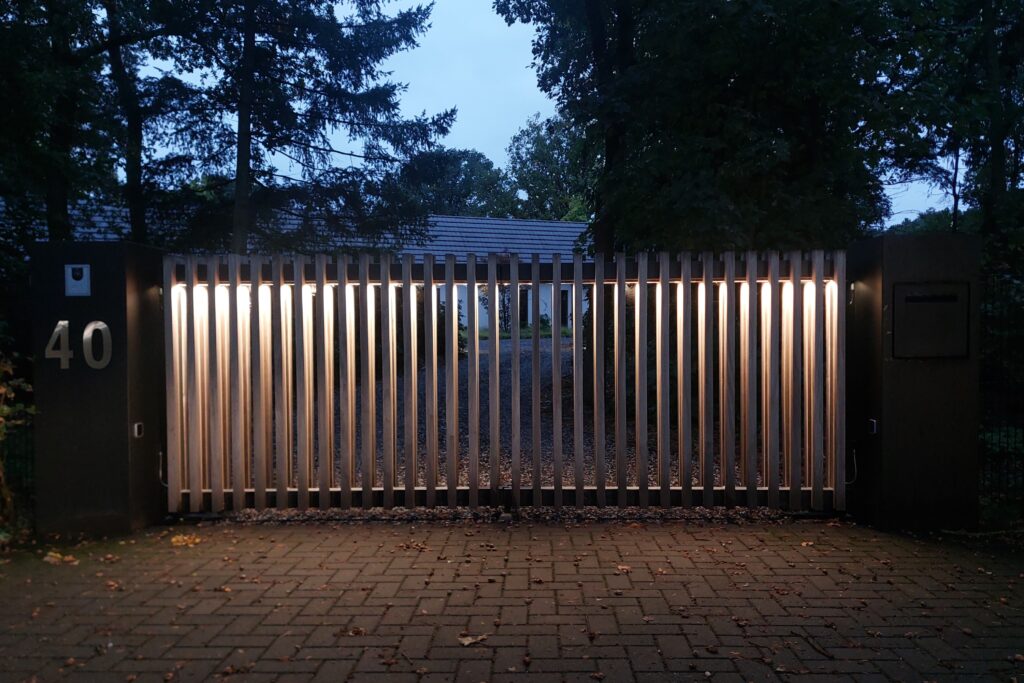 Een houten poort met sfeerverlichting in de vleugels. Een mooie en praktische verlichting welke opgaat in het model van de poort.
