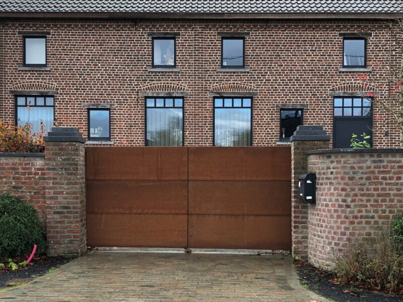 http://Cortenstaal%20dichte%20draaipoort%20tussen%202%20gemetselde%20pilasters.