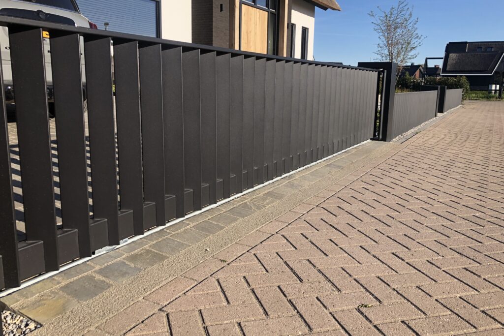 Moderne strakke schuifpoort van brede schuine lamellen. Passend bij een strakke tuin en moderne woning.
